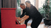 a man and a woman are playing a pink piano in front of a window with the letters h & z on the bottom