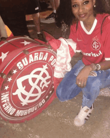 a woman wearing a red shirt that says anrisul sits next to a red drum