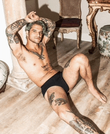 a shirtless man with tattoos is laying on the floor with his legs crossed