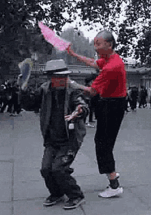 a man in a red shirt is standing next to a man in a hat who is holding a pink umbrella .