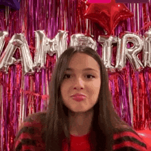 a woman is making a funny face in front of a wall with balloons that spell out the word vampire .