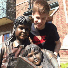 a boy and a girl are posing for a picture next to a statue of a boy and a girl reading a book .