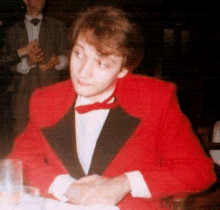 a young man in a red suit and bow tie is sitting at a table .