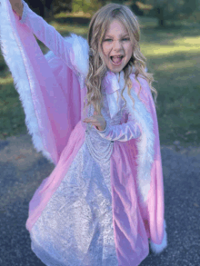 a little girl dressed in a pink and white dress with a white fur cape