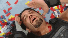 a man with a beard is laying on the ground with his eyes closed and confetti falling around him