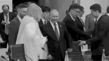 a man in a suit and tie is shaking hands with a woman in a white dress in a black and white photo .