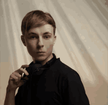 a young man in a black shirt holds a pair of headphones to his ear