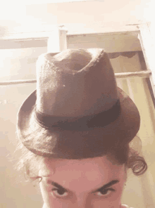 a woman wearing a fedora hat looks at the camera with a serious look on her face