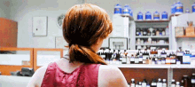 a woman in a red tank top is standing in front of a pharmacy counter filled with bottles of medicine .