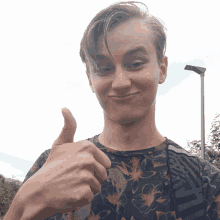 a young man giving a thumbs up with a floral shirt on