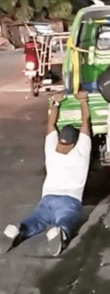 a man is kneeling down on the side of the road while carrying a green bag on his head .