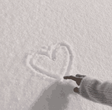 a person draws a heart in the snow with their finger