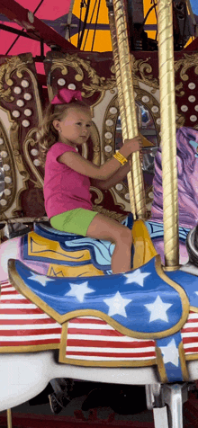 a little girl in a pink shirt is riding a carousel