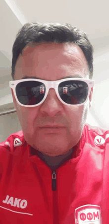 a man wearing white sunglasses and a red jako jacket