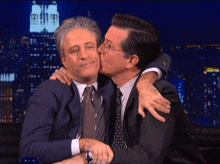 a man kisses another man on the cheek in front of an empire state building