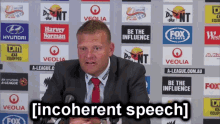 a man in a suit and tie is giving a speech in front of a wall of advertisements including veolia and fox