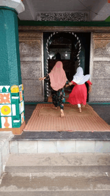 two women are entering a building with arabic writing on the wall