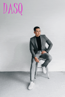 a man in a suit is sitting on a stool in front of a wall with dasq written on it