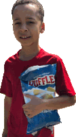 a young boy in a red shirt holds a bag of duffles chips