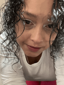 a woman with curly hair wearing a white shirt looks at the camera