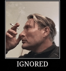 a man is smoking a cigarette with a poster that says ignored on it .