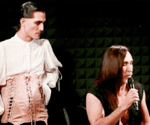 a man in a corset is standing next to a woman in a microphone .