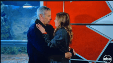 a man and a woman are hugging in front of a red and white abc sign