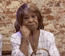 an older woman is sitting at a table with her hand on her chin and a purse .