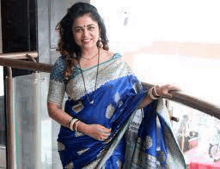 the woman is wearing a blue saree and standing on a balcony .