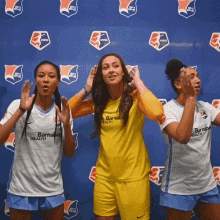 three female soccer players are posing for a photo in front of a blue wall with logos for barnacle health on it