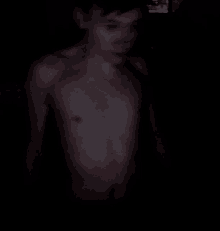 a shirtless man is standing in the dark with a blurry background