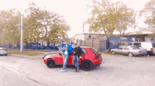 two men standing next to a red car in a parking lot with a sign that says " automovka " on it