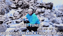 a man in a blue shirt sits on a pile of rocks with the words " stay tuned " above him