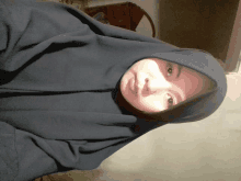 a woman wearing a hijab looks at the camera with her eyes closed