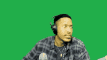 a man wearing headphones and a plaid shirt on a green screen .