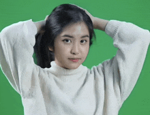 a woman in a white sweater is holding her hair in front of a green screen