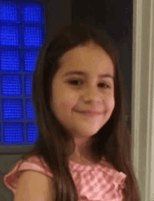 a little girl is smiling and looking at the camera while wearing a pink dress .