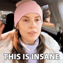 a woman wearing a pink beanie is sitting in a car and says this is insane