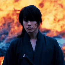 a man in a black kimono holds a sword in front of a fire