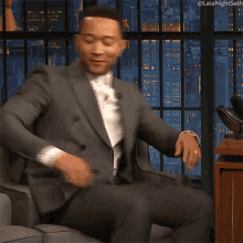 a man in a suit is sitting on a couch with his legs crossed and the hashtag latenightseth is above him