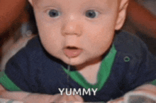 a baby is laying down with his mouth open and the word yummy is on the bottom of his face .