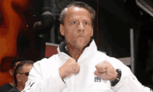 a man in a white jacket is standing in a boxing ring with his fists in the air .