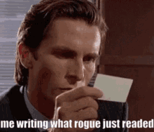 a man in a suit is holding a piece of paper in his hand with the words `` me writing what rogue just readed '' .