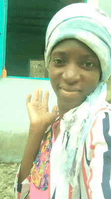 a woman wearing a head scarf and a striped shirt waves her hand in front of a window