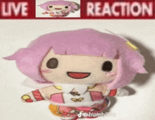 a stuffed doll with pink hair is sitting in front of a banner that says live reaction