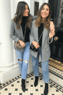 two women standing next to each other wearing jeans and jackets