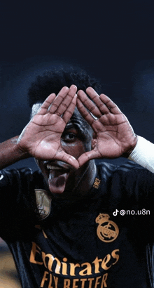 a man wearing a black emirates fly better jersey making a heart with his hands