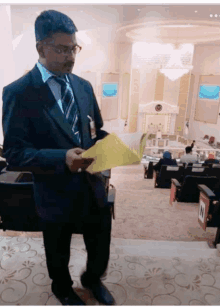 a man in a suit and tie holds a piece of paper in front of a large room