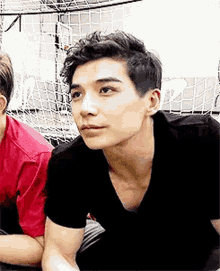 a young man in a black shirt is sitting in front of a basketball net and looking at the camera .