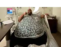 a very fat man in a hospital bed giving a thumbs up